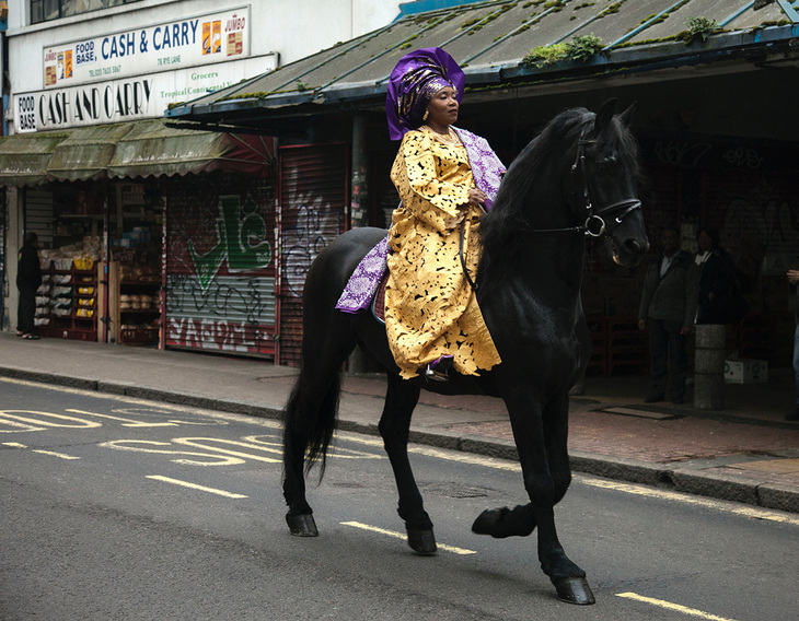 A woman in bright Nigerian clothes riding a horse down a high street