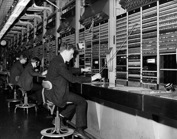 A man in a suit sits at a switchboard