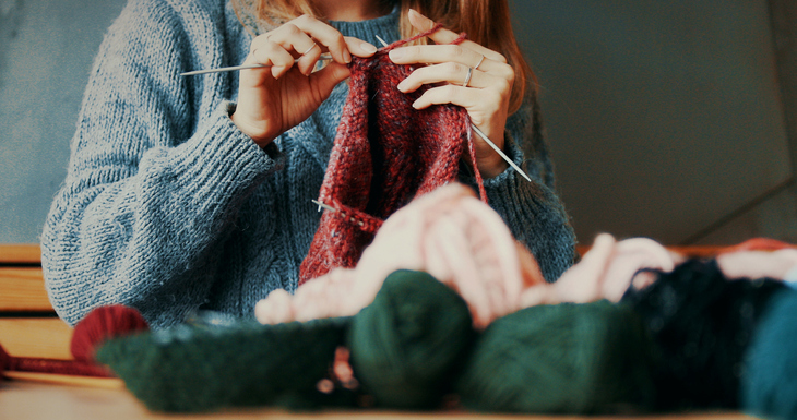 Close up of someone knitting something - they're wearing a blue knitted jumper