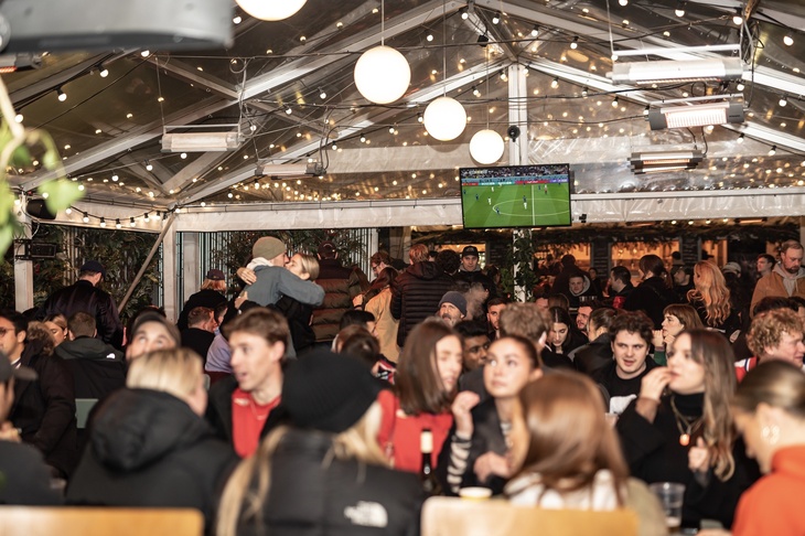 A crowd of people, with a TV screen showing sport behind them