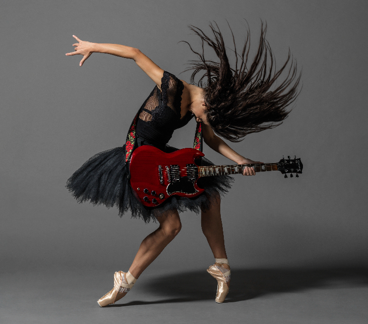 A ballerina in black tutu and leotard playing a red electric guitar