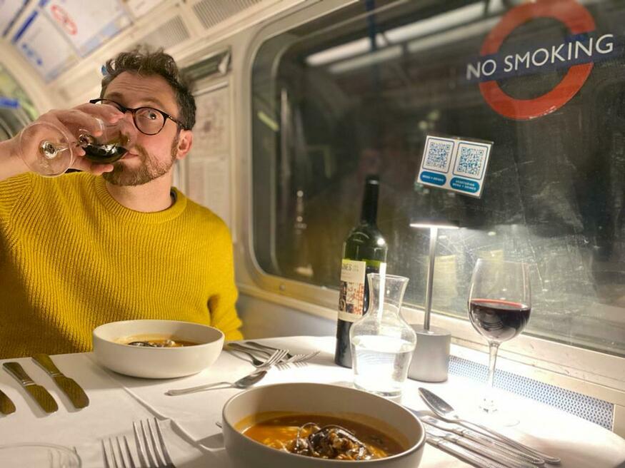 Tube Supperclub: A man in a yellow sweater drinking wine at a dinner table in a tube carriage