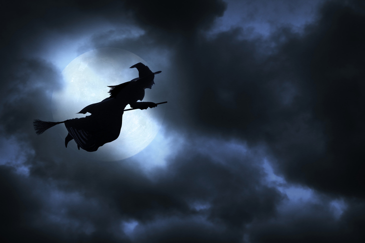 Silhouette of a witch flying against the moon