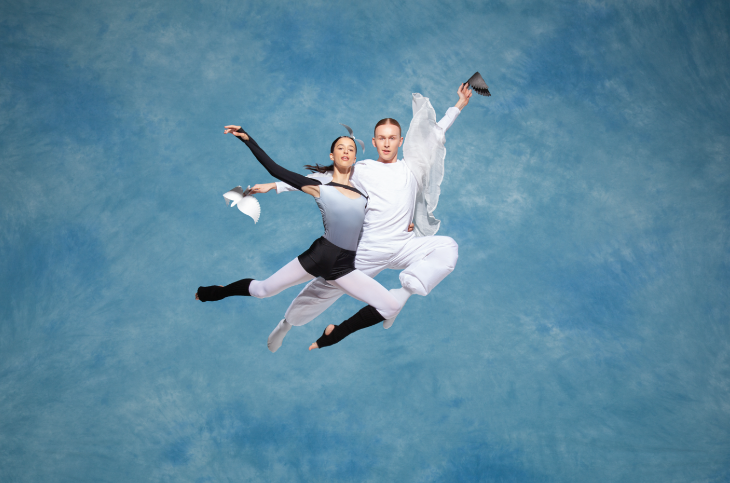A male and female ballet dancer entwined together in a leap