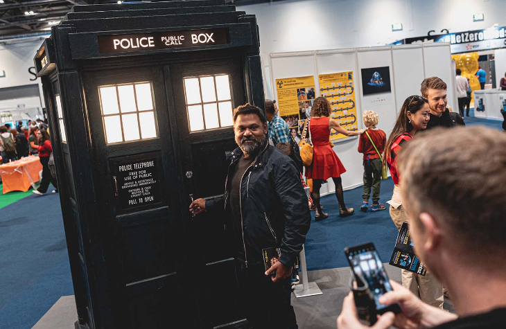A man posing in front of a replica TARDIS while someone takes a photo