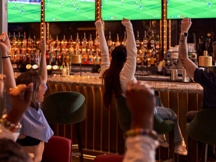 People cheering in front of screens in a sports bar